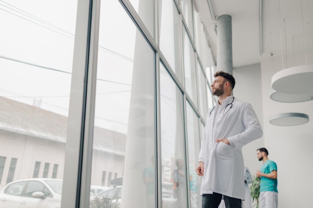 Doctor looking out window in modern hospital corridor